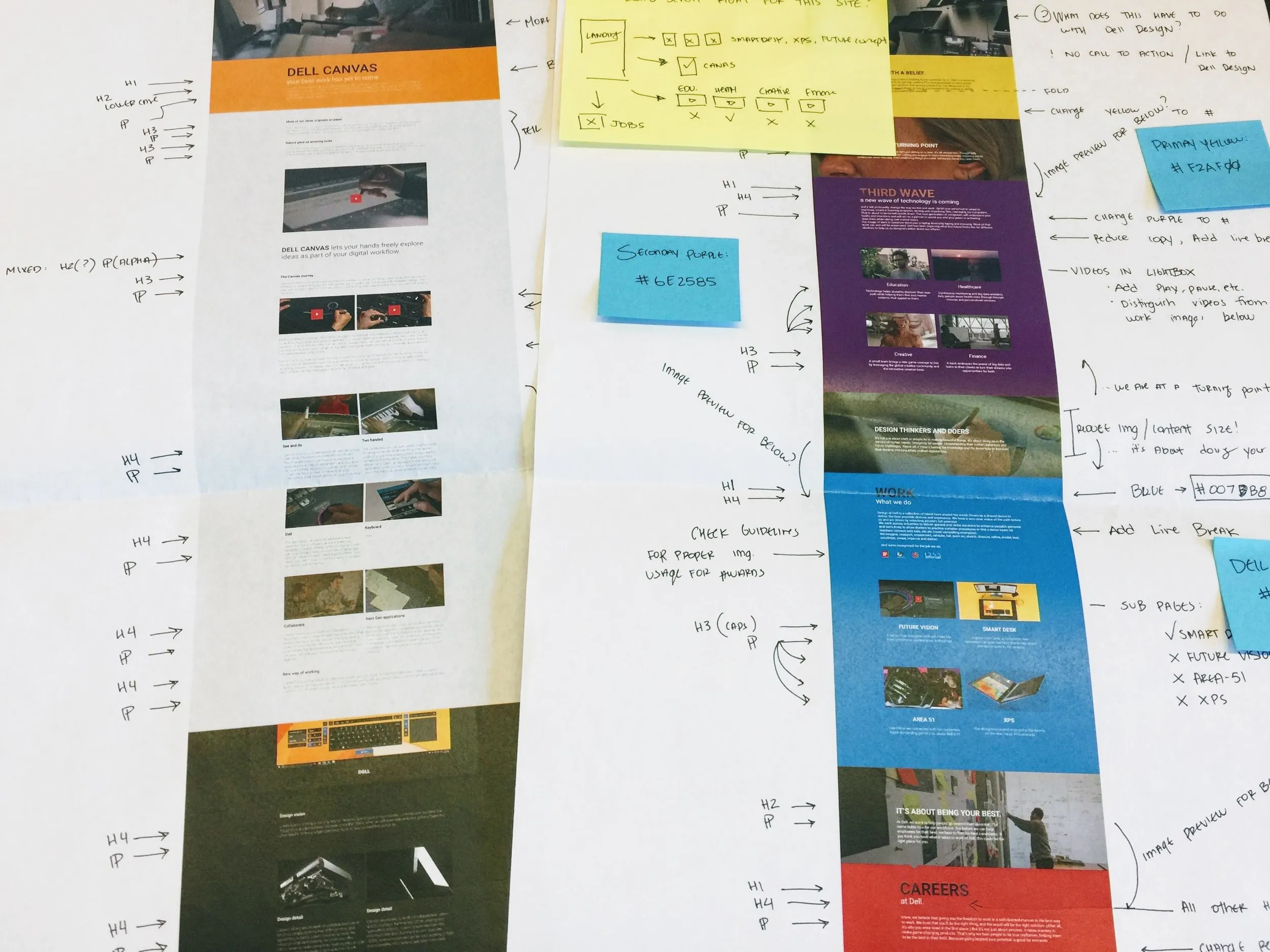 Printed page designs taped to a table, marked up by hand with heading levels, color values and sticky notes.